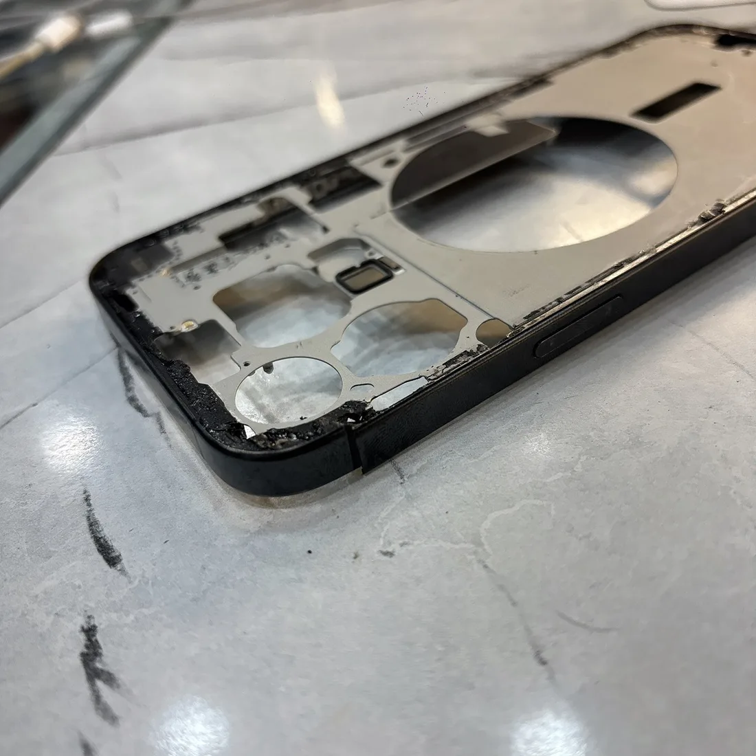 台南 iPhone 15 Pro Max 拆下來的變形舊中框,邊緣可見撞擊變形與殘膠
